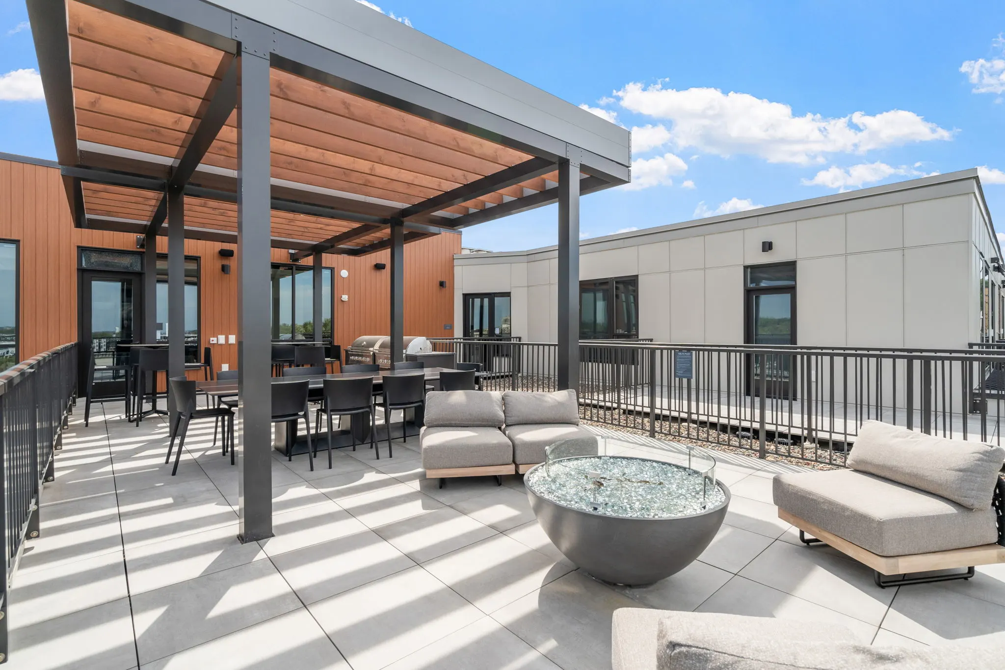 Rooftop lounge at The Townline Apartments with pergola, fire pit, cushioned seating, and dining area.