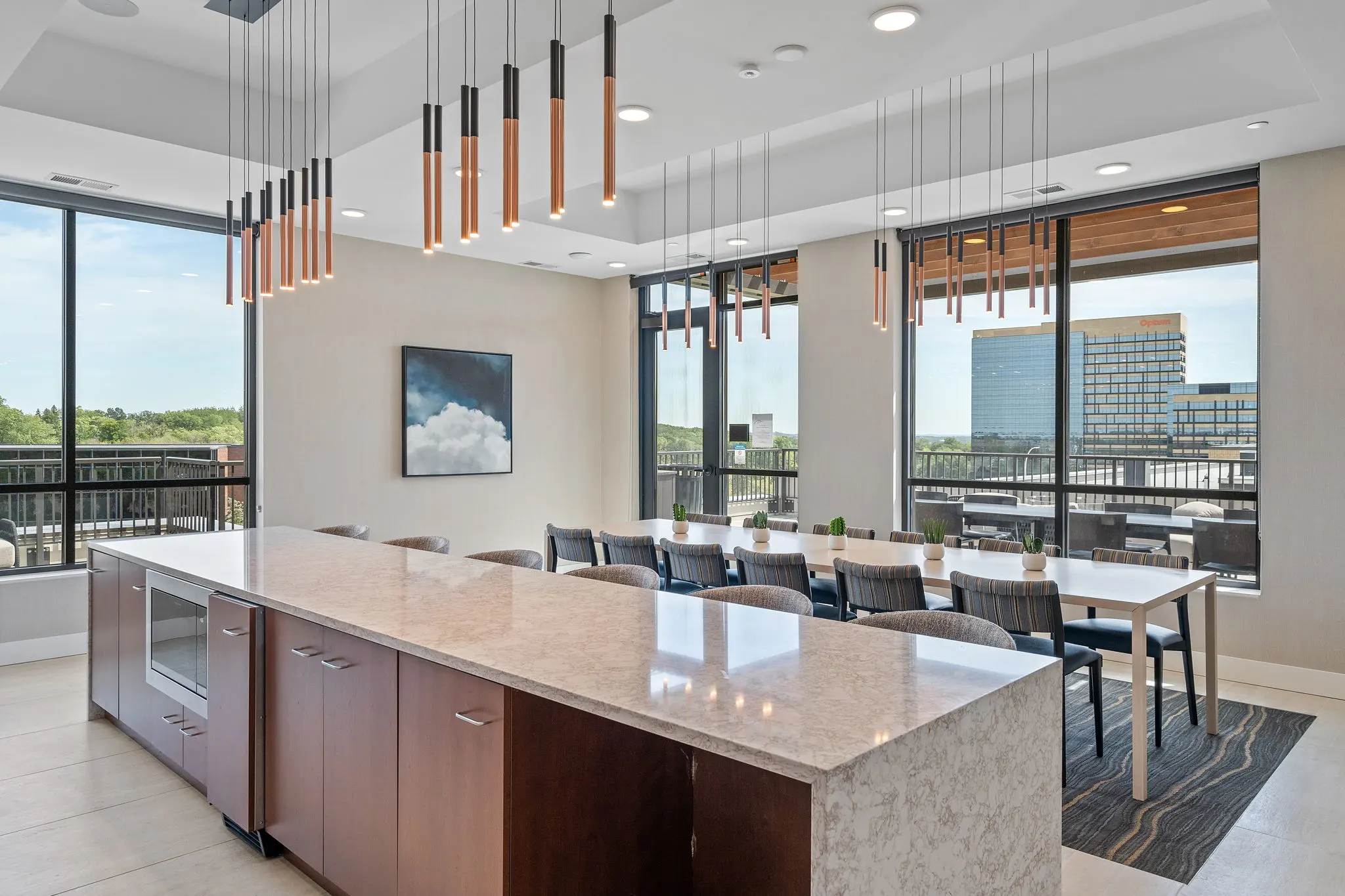Sky lounge dining area at The Townline Apartments with large island, communal table, and floor-to-ceiling windows.