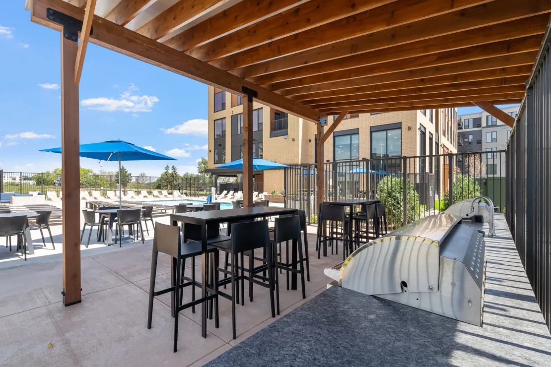 Covered outdoor grilling area at The Townline Apartments with bar-height seating and pool views.