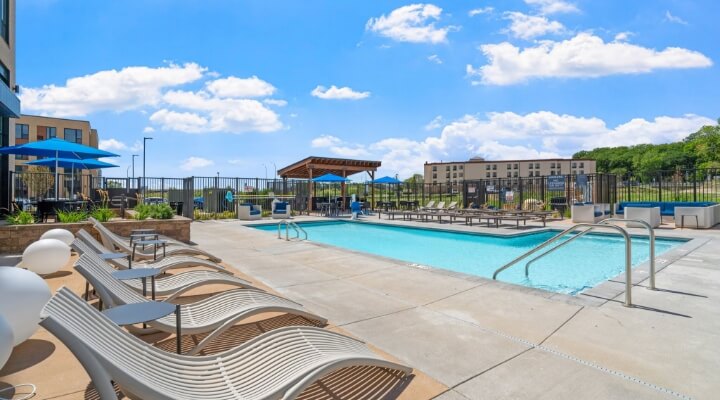 Outdoor pool at The Townline Apartments with sundeck seating, umbrellas, and lounge chairs.