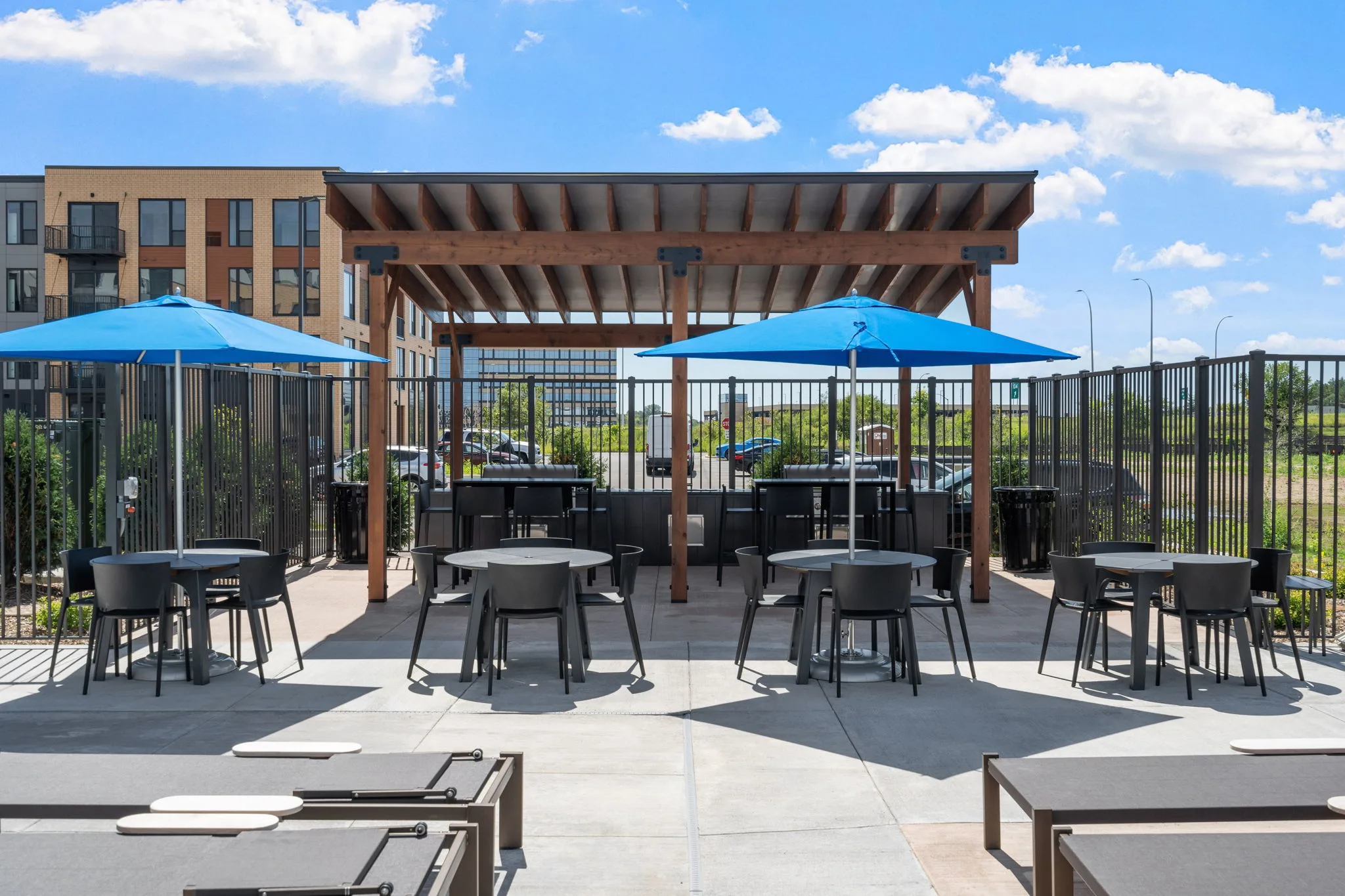 Pergola-covered outdoor grilling area at The Townline Apartments with tables, umbrellas, and poolside seating.