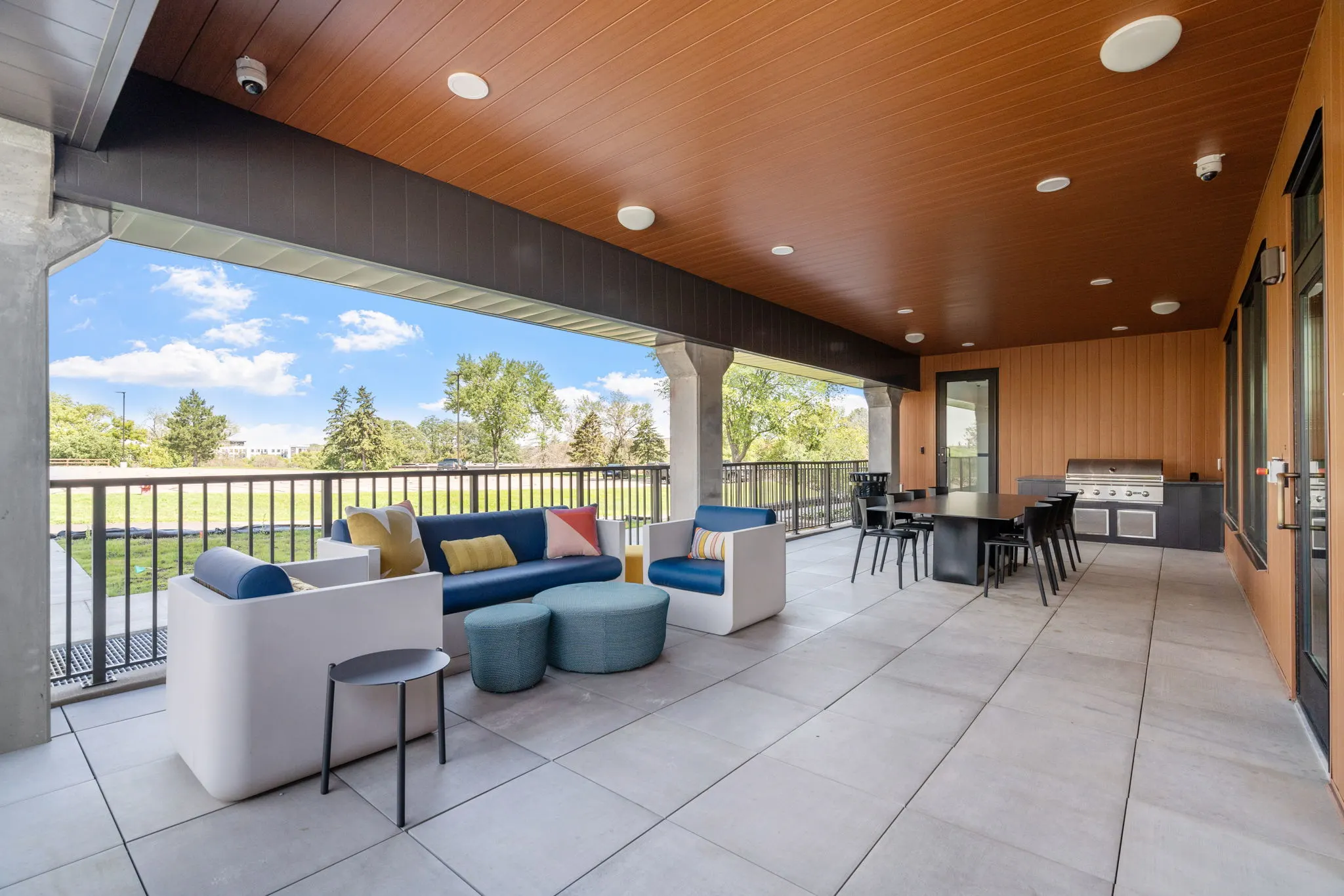 Covered outdoor lounge at The Townline Apartments with grill station, dining area, and cushioned seating.
