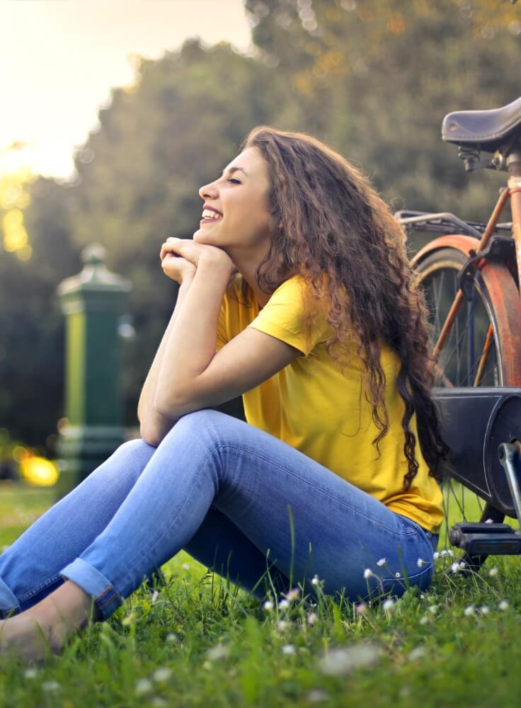Woman sitting on the grass beside a bicycle, representing the neighborhood lifestyle near The Townline Apartments.