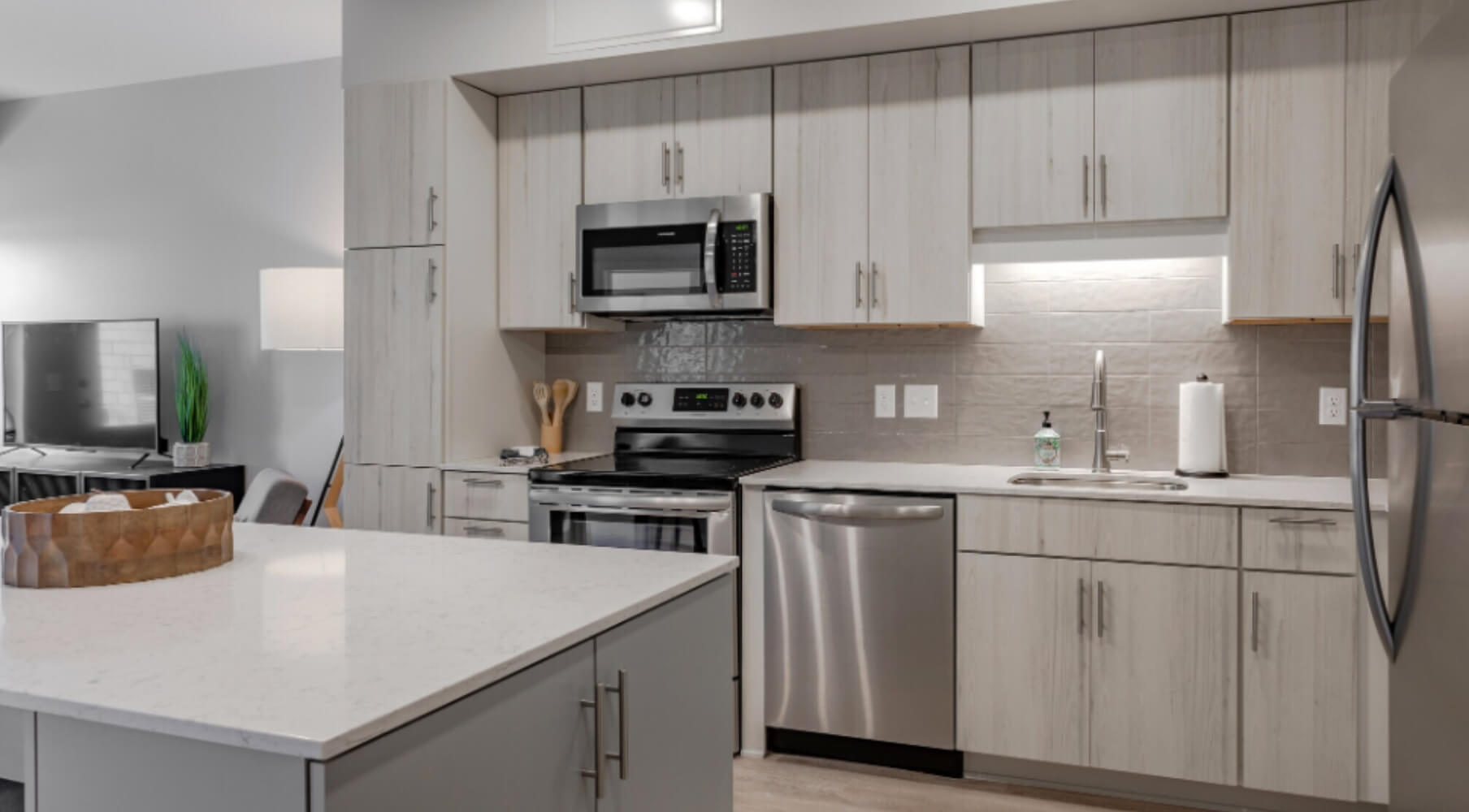 Modern apartment kitchen at The Townline Apartments with light wood cabinetry, white island countertops, and stainless steel appliances.