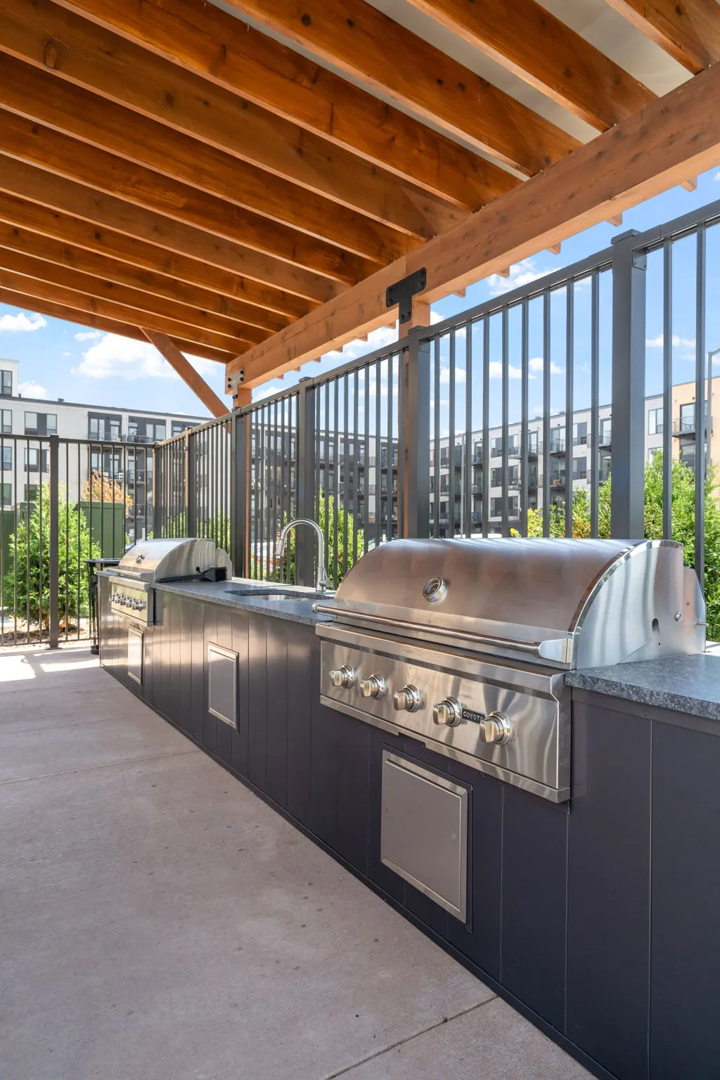 Outdoor grill station at The Townline Apartments beneath a wood pergola with built-in grills and prep space.