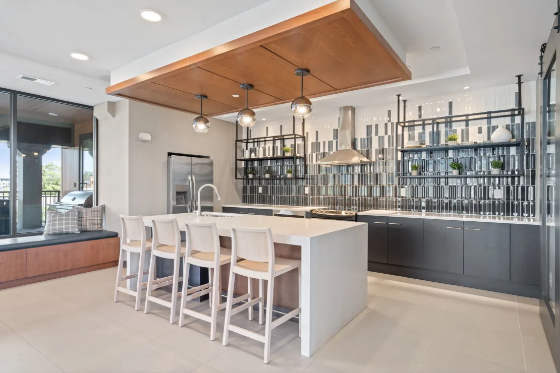 Community kitchen at The Townline Apartments with large island seating, pendant lighting, and modern tile backsplash.
