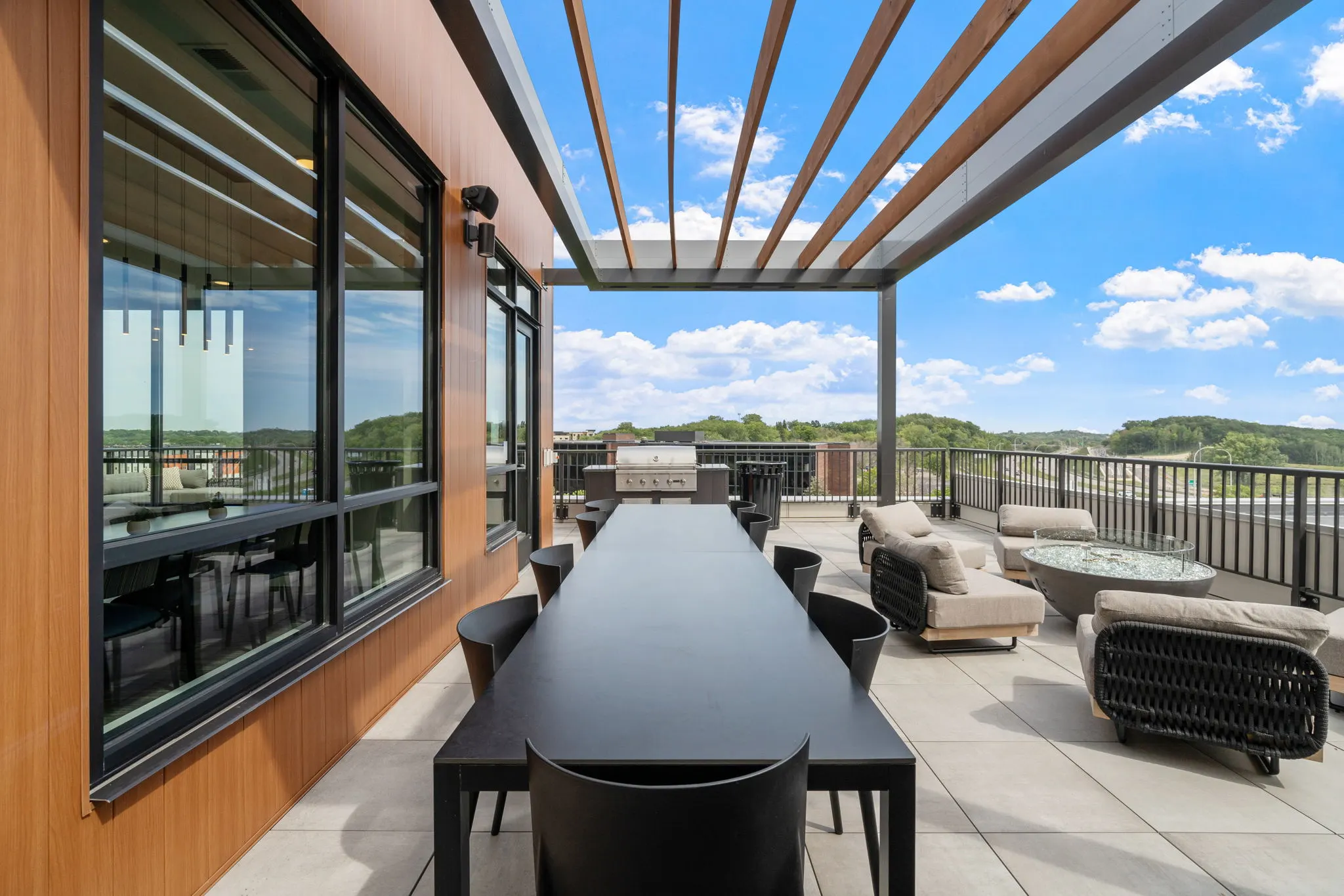 Rooftop patio at The Townline Apartments with long dining table, lounge seating, and built-in grill.