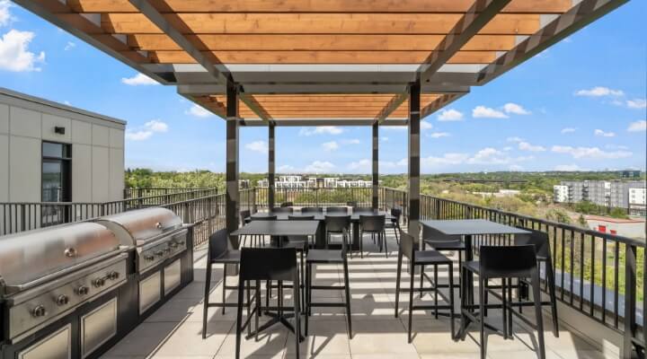 Rooftop patio at The Townline Apartments with pergola, grilling stations, dining tables, and skyline views.