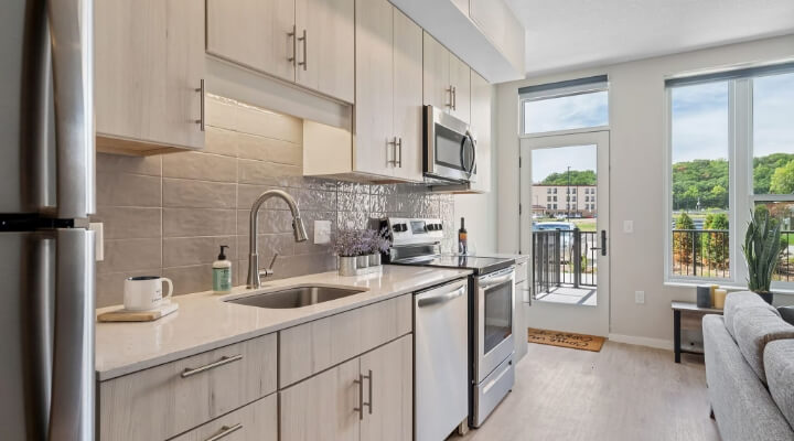 Apartment kitchen at The Townline Apartments with stainless steel appliances, light wood cabinetry, and balcony access.