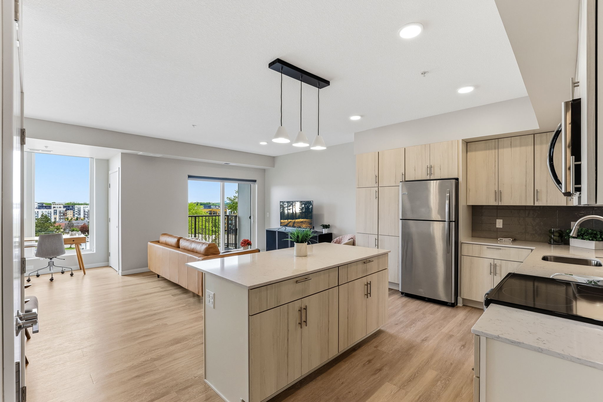 Modern apartment kitchen at The Townline Apartments with light wood cabinetry, white island countertops, and stainless steel appliances.