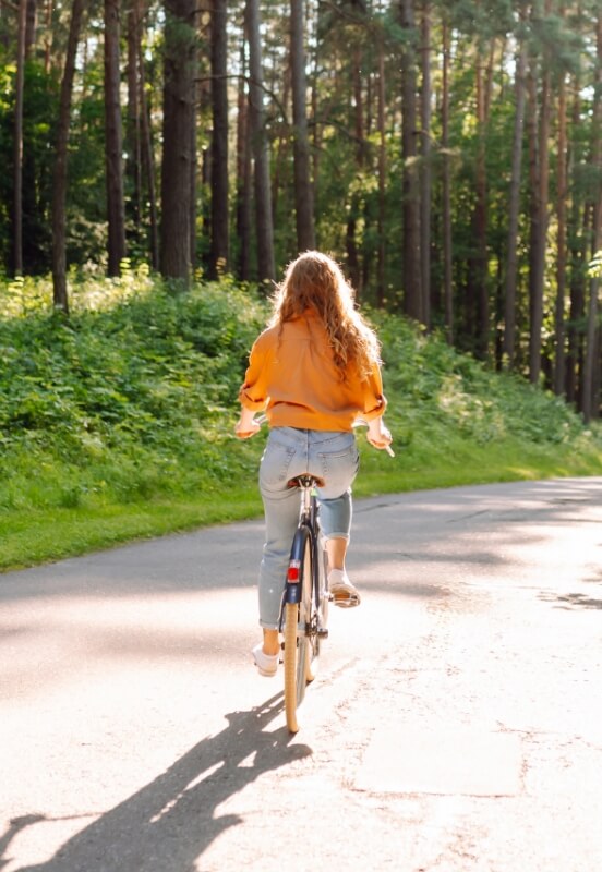 Woman riding a bicycle on a paved trail through a wooded area