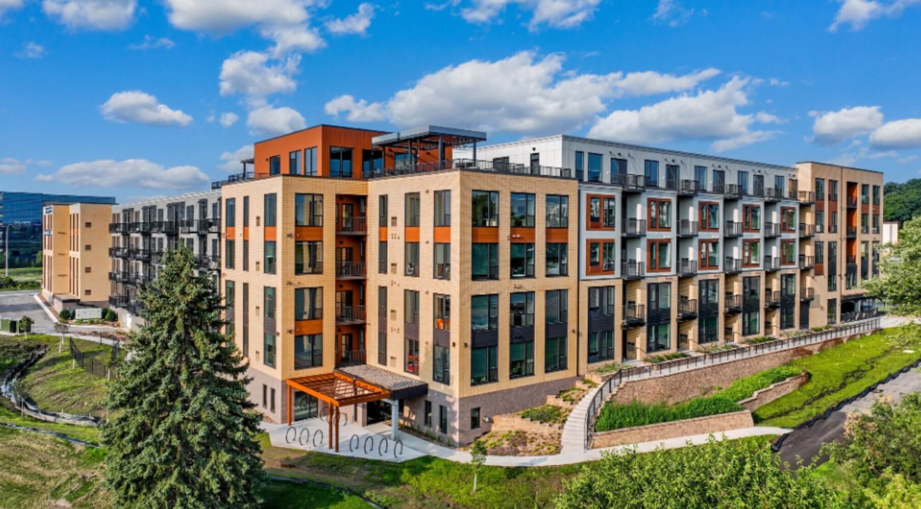 Aerial view of The Townline Apartments exterior showing the multi-story apartment building, balconies, and landscaped grounds under a blue sky.