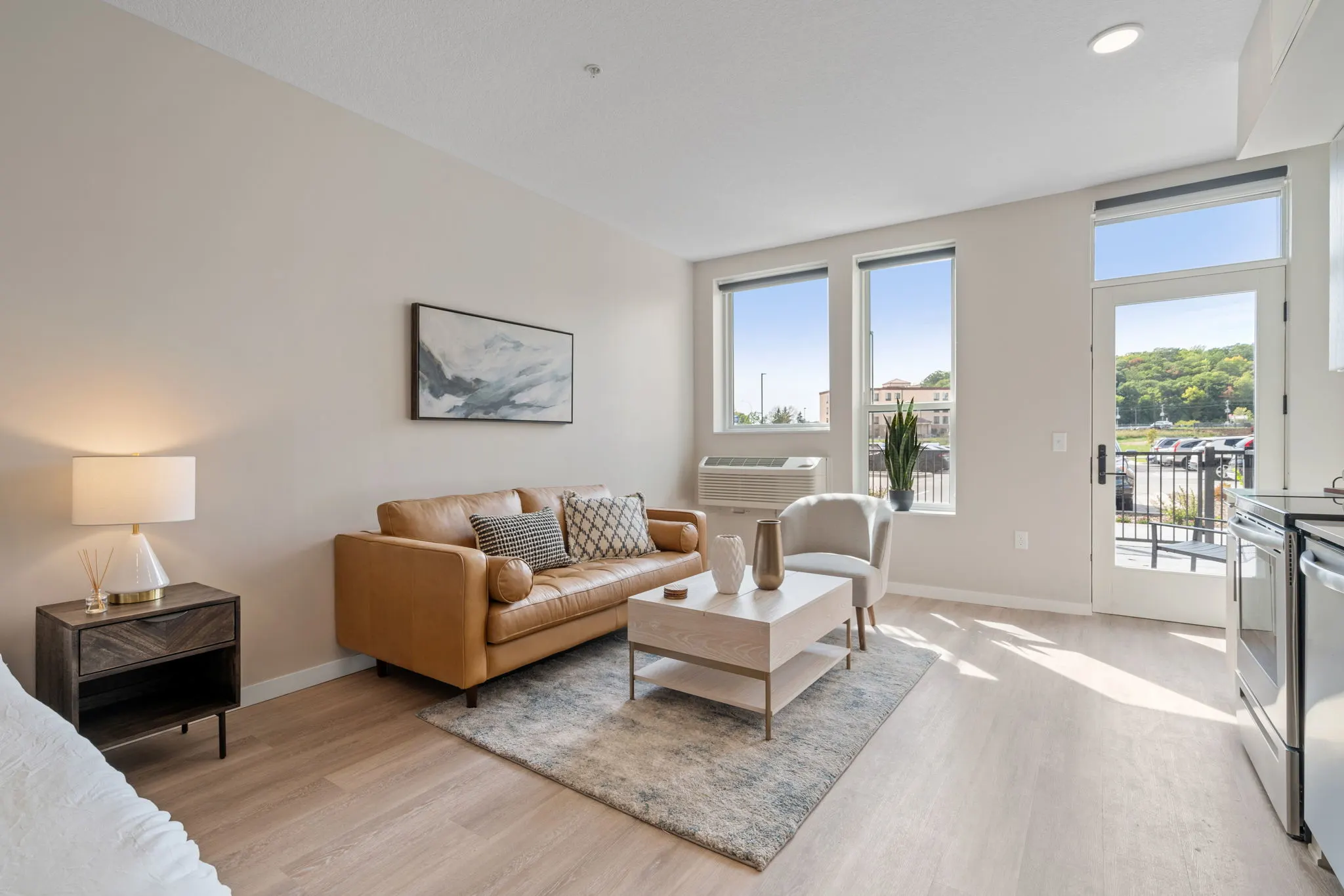 Studio living area at The Townline Apartments with sofa, accent chair, large windows, and balcony access.