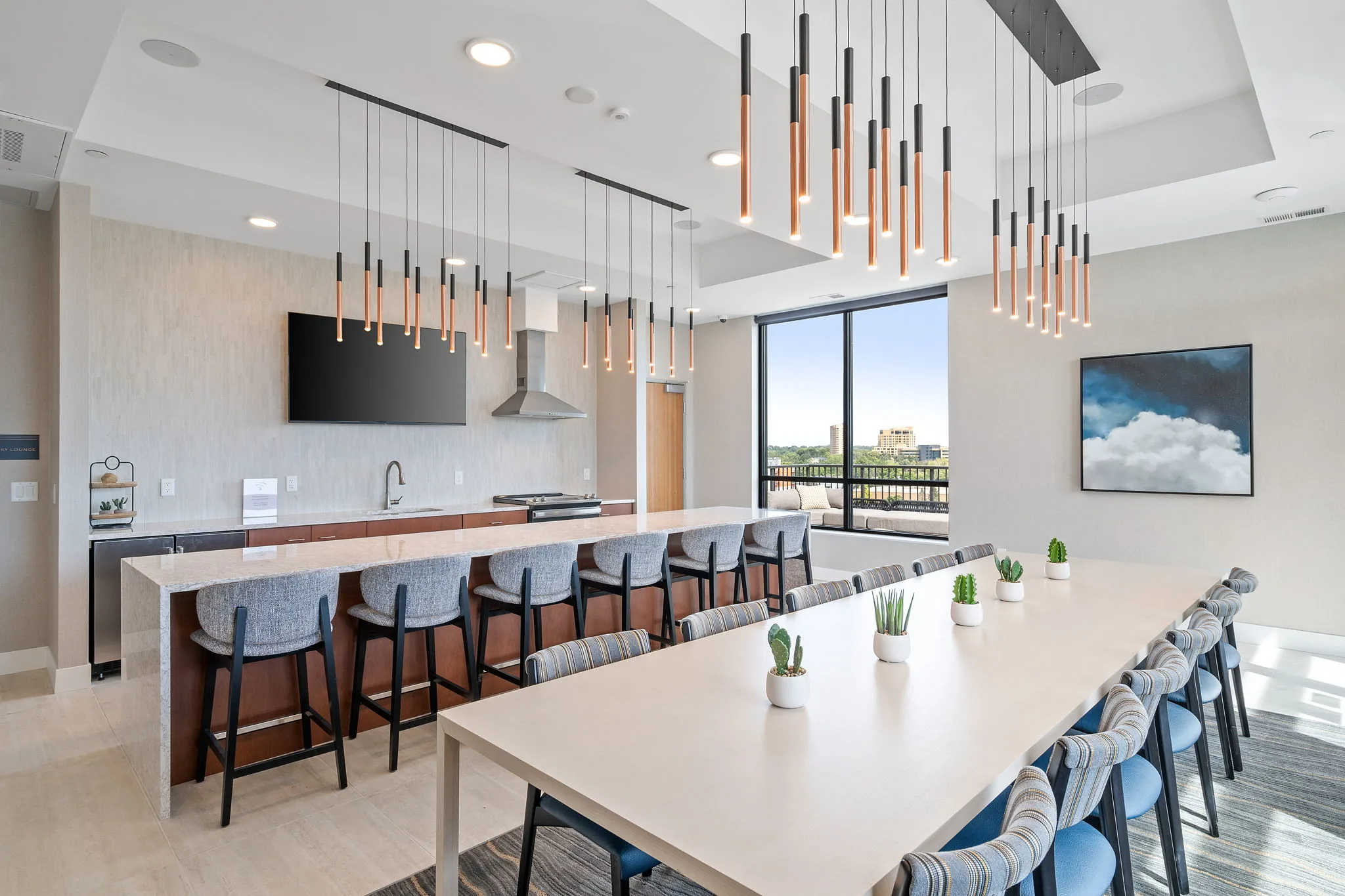 Sky lounge at The Townline Apartments with long dining table, bar seating, pendant lighting, and city views.