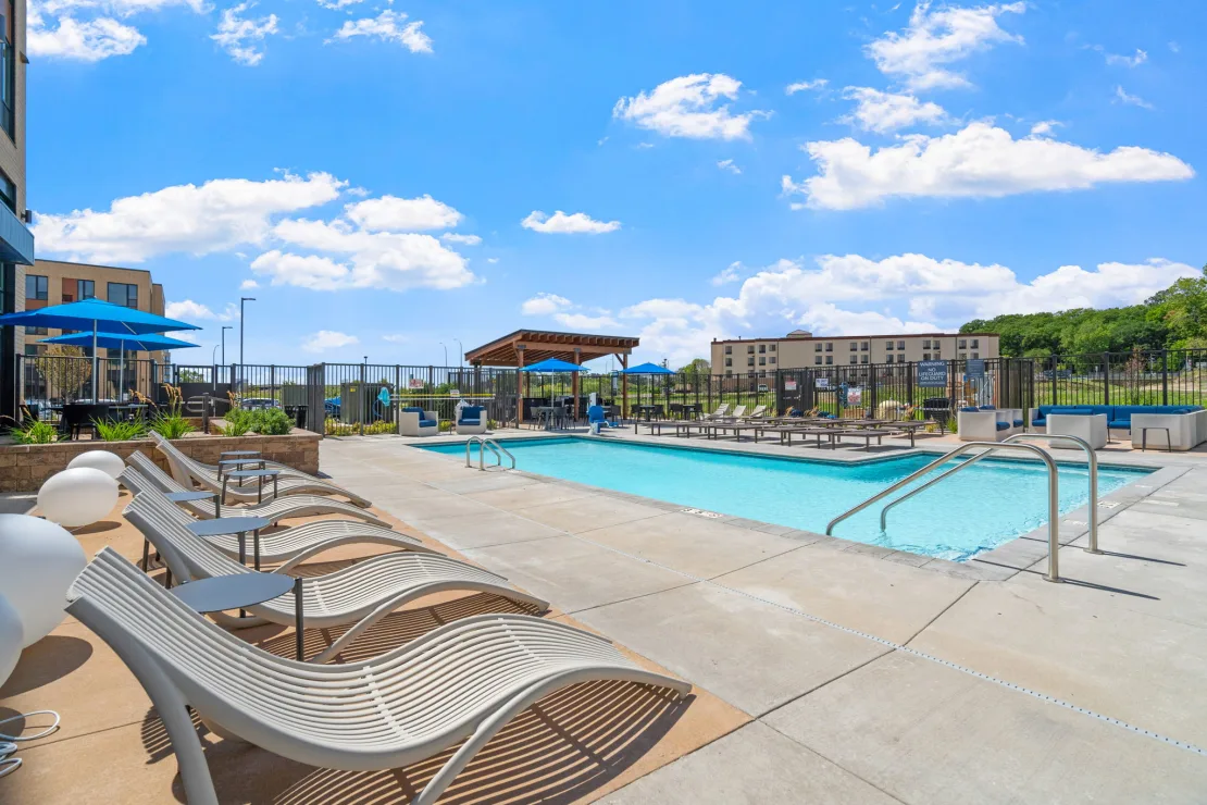 Outdoor pool at The Townline Apartments with lounge chairs, sundeck seating, and community building views.
