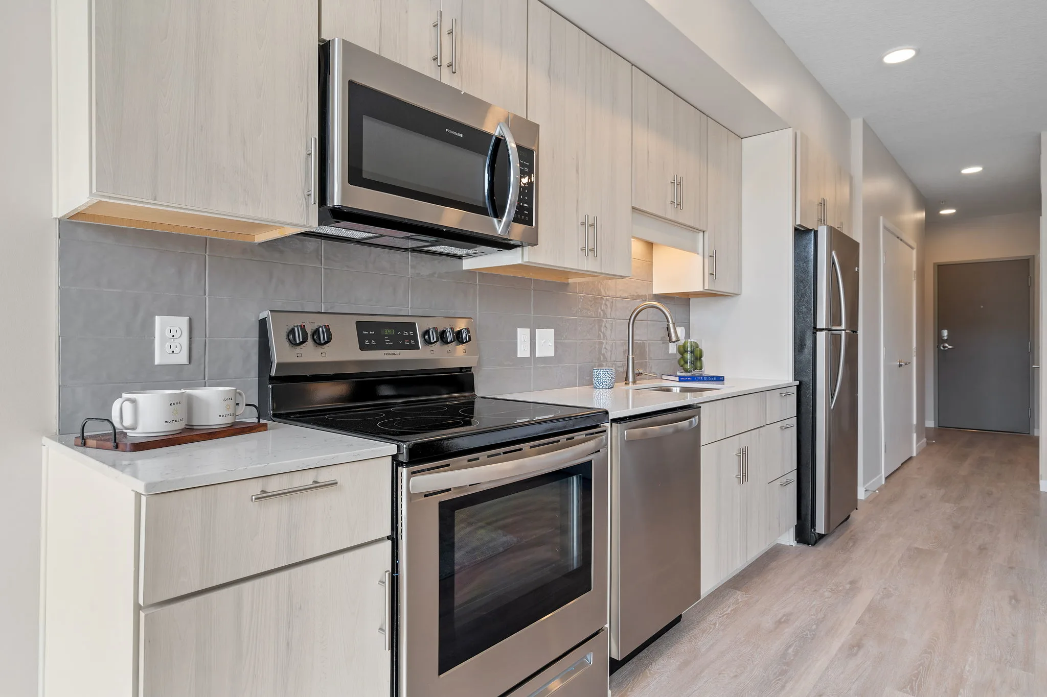 Apartment kitchen at The Townline Apartments with stainless steel appliances, light wood cabinetry, and quartz countertops.